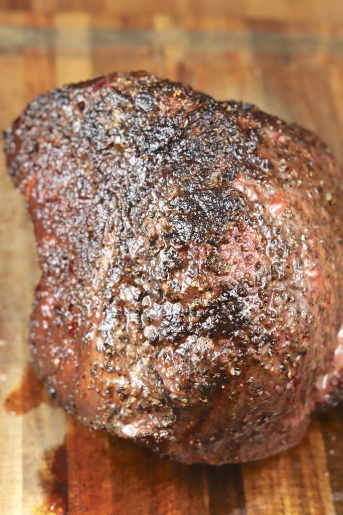 Pepper crusted rump roast grilled, resting on cutting board. 