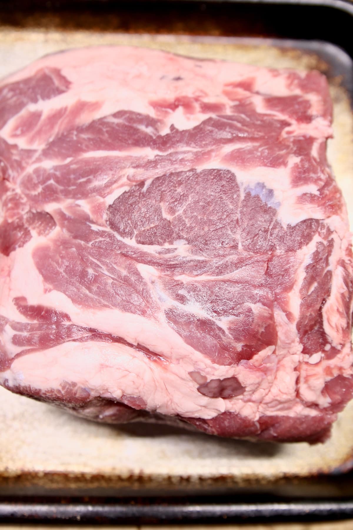 Raw pork butt on a sheet pan.