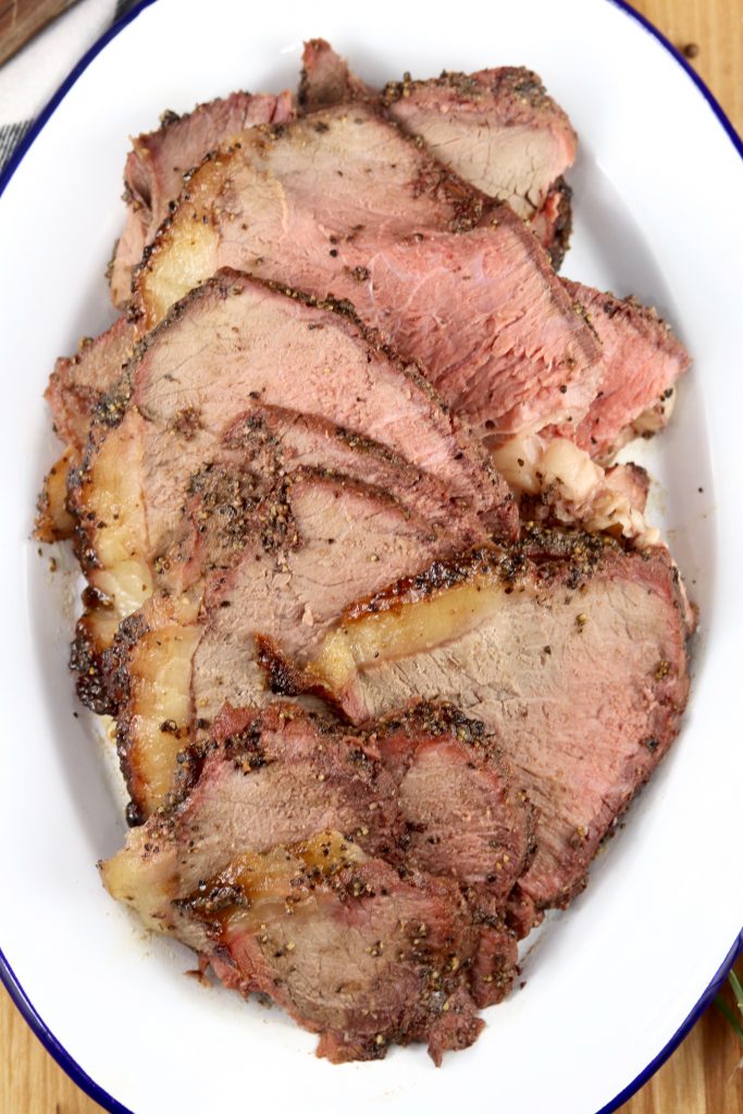 Thinly sliced roast beef with peppered crust on a white platter
