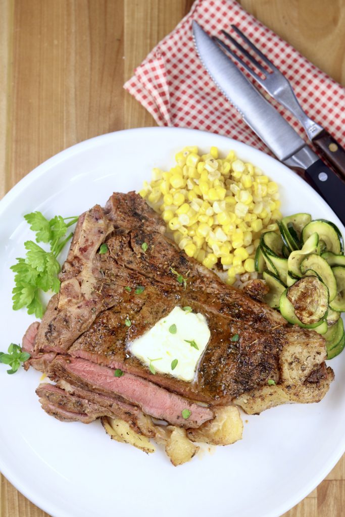 Grilled T-Bone Steaks with a pat of butter, corn and zucchini