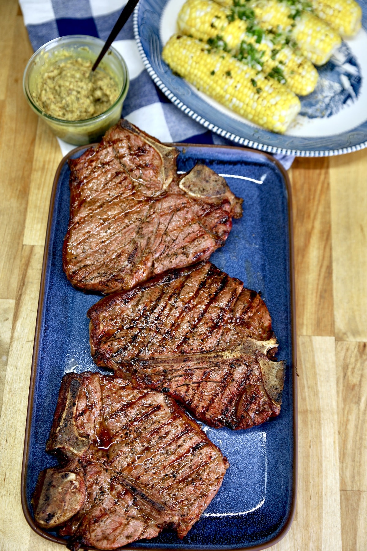 3 grilled t-bone steaks with platter of corn and steak butter.