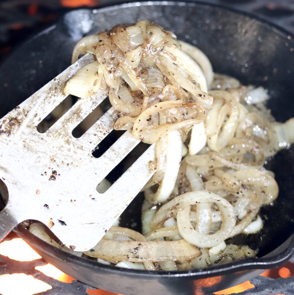 Grilled onions in a skillet stirring with spatula
