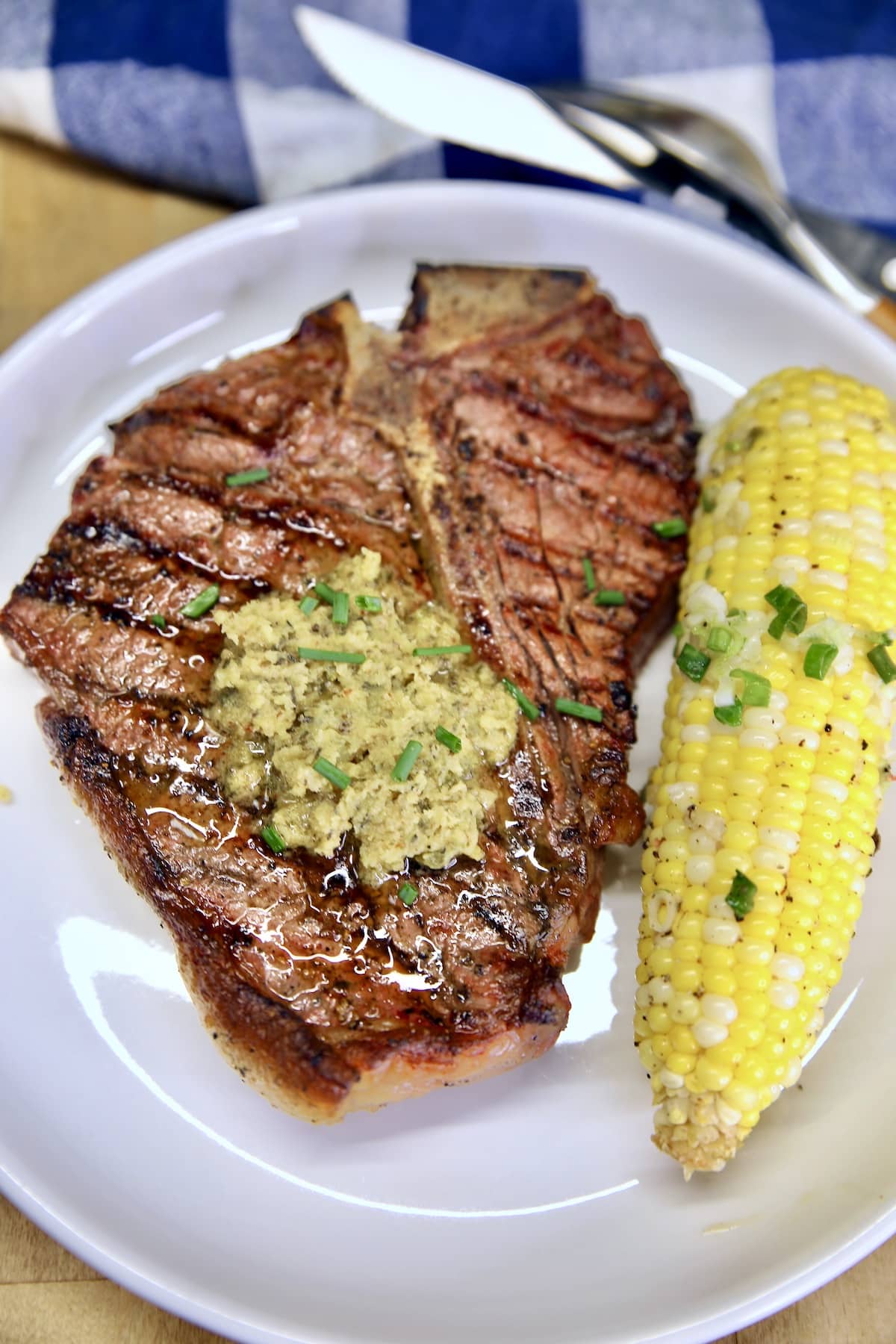 T-Bone steak on a plate with steak butter, corn on the cob.
