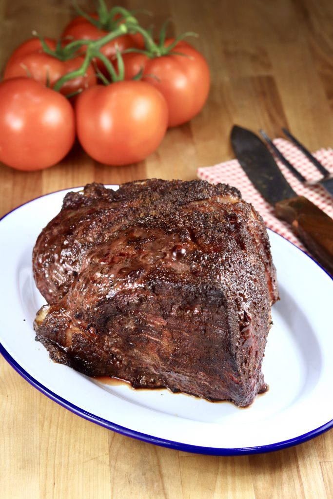 Grilled Rump Roast on a platter with ripe tomatoes in background
