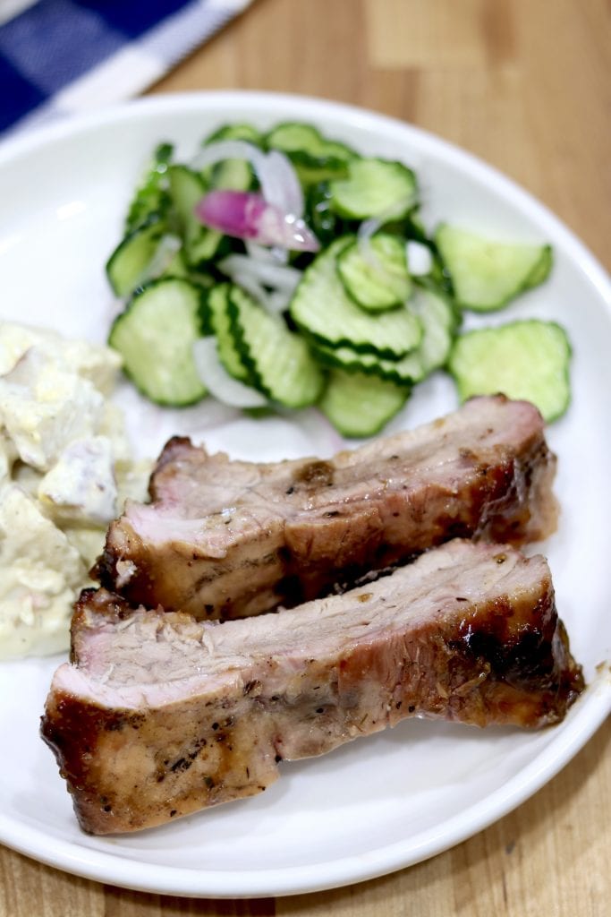 Plate of 2 sliced baby back ribs with potato salad and cucumber salad