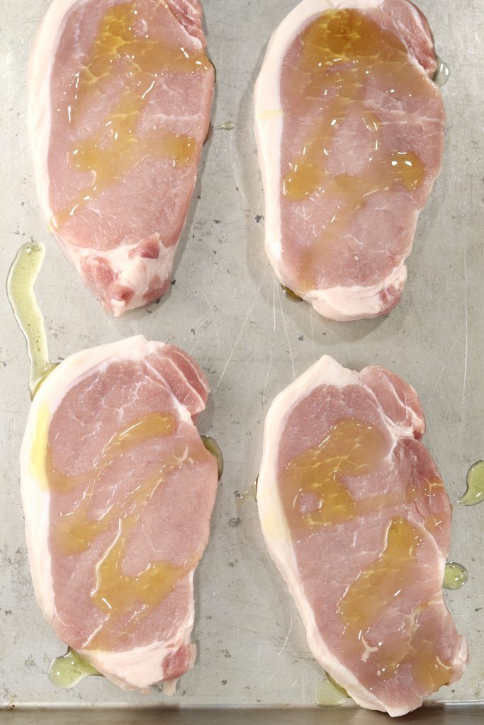 Boneless pork chops on a baking sheet, drizzled with olive oil