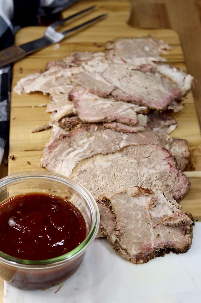 Sliced brisket on a cutting board with bbq sauce
