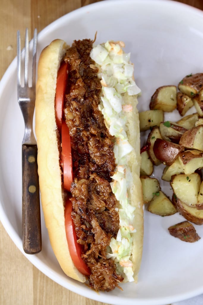 Brisket Po Boy with tomatoes and coleslaw on a plate with roasted potatoes