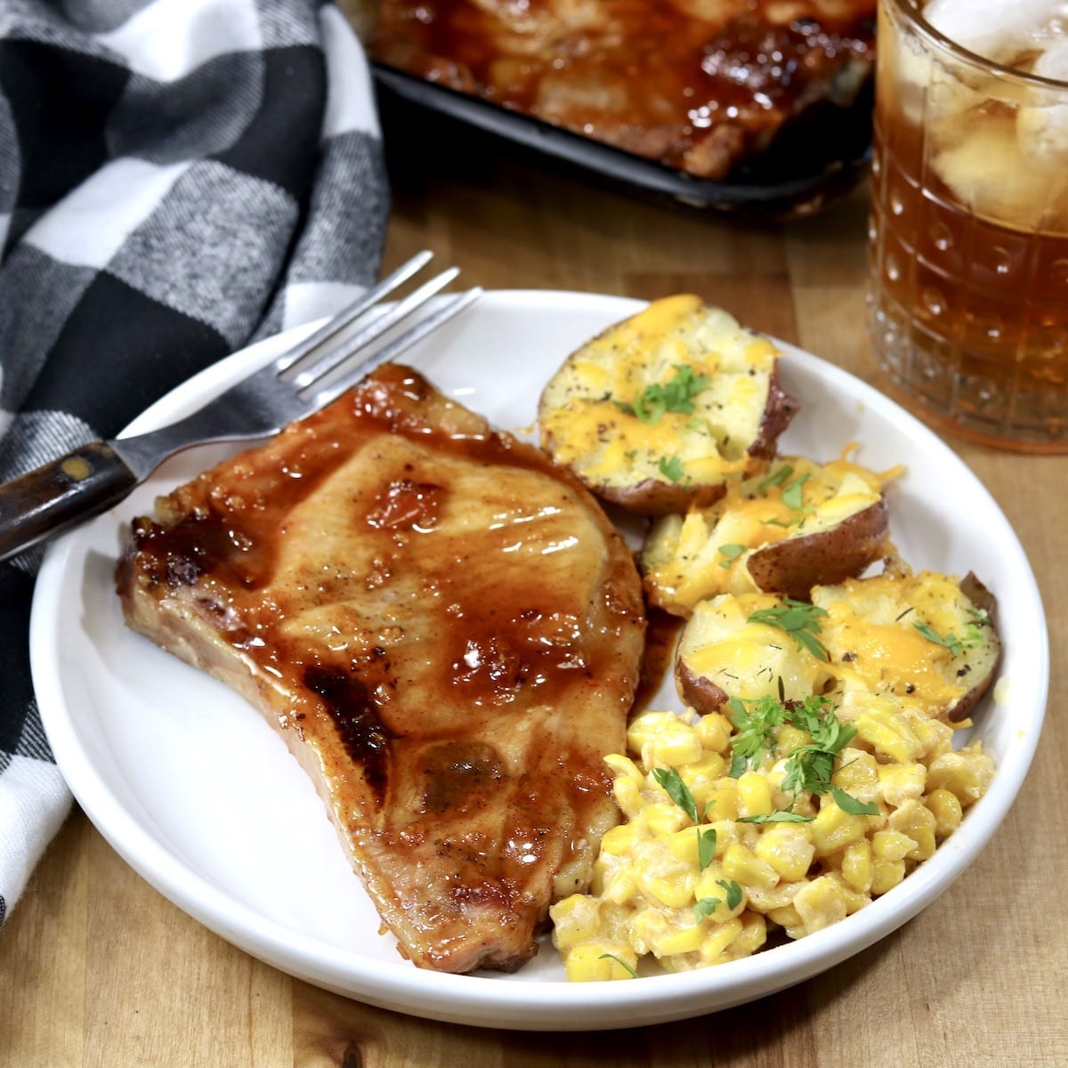 Peach BBQ Pork Chop on a white plate with potatoes and corn