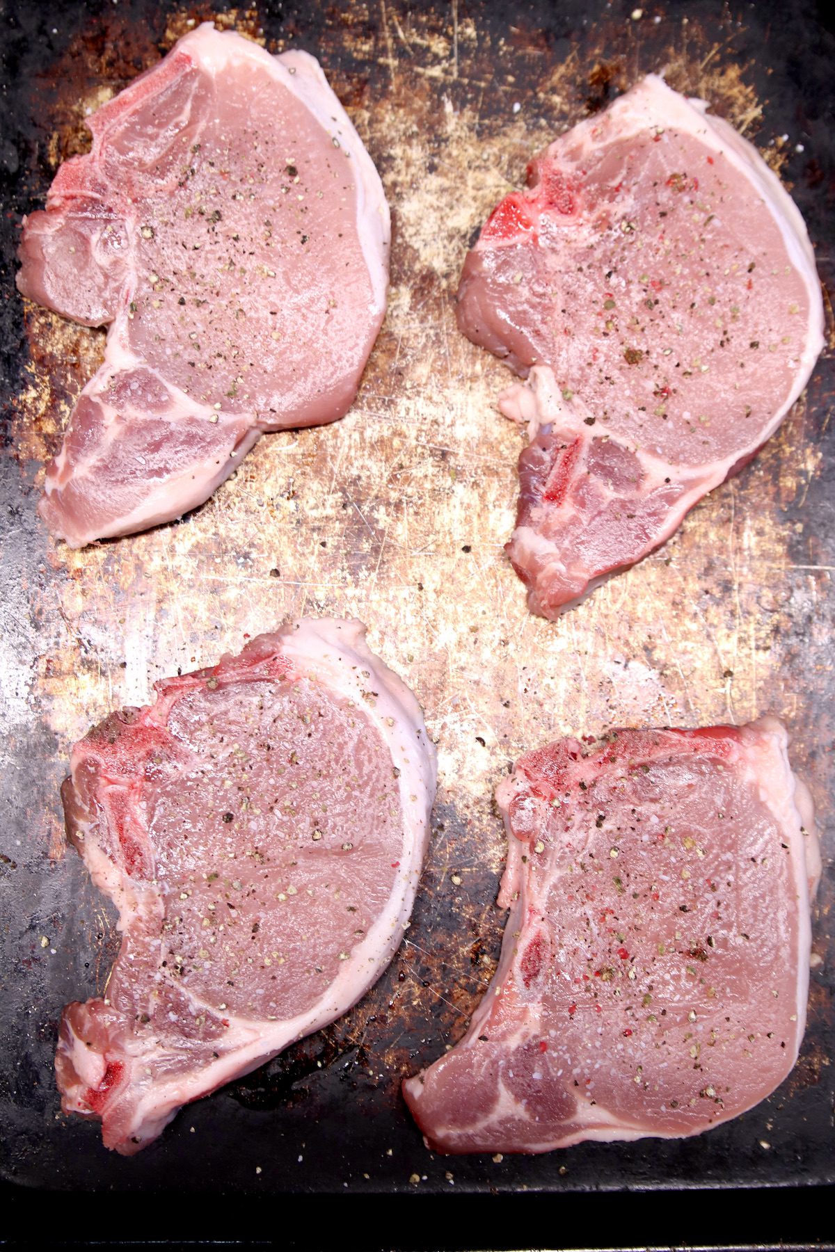 4 bone-in pork chops on a rimmed baking sheet.