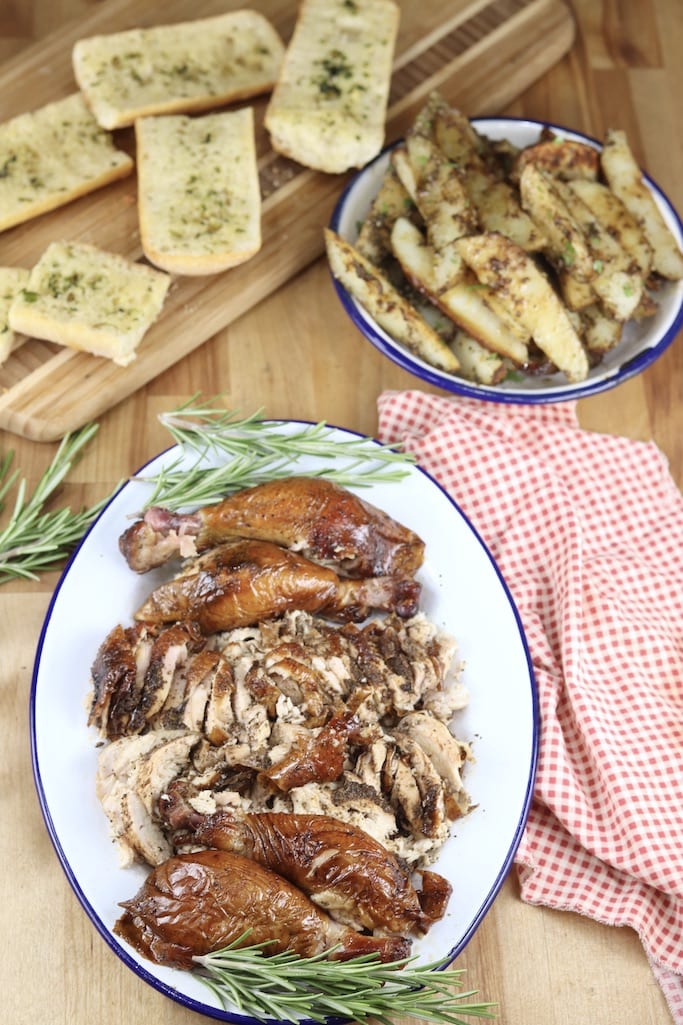 smoked chicken on a platter, board with garlic bread slices and bowl of potato wedges