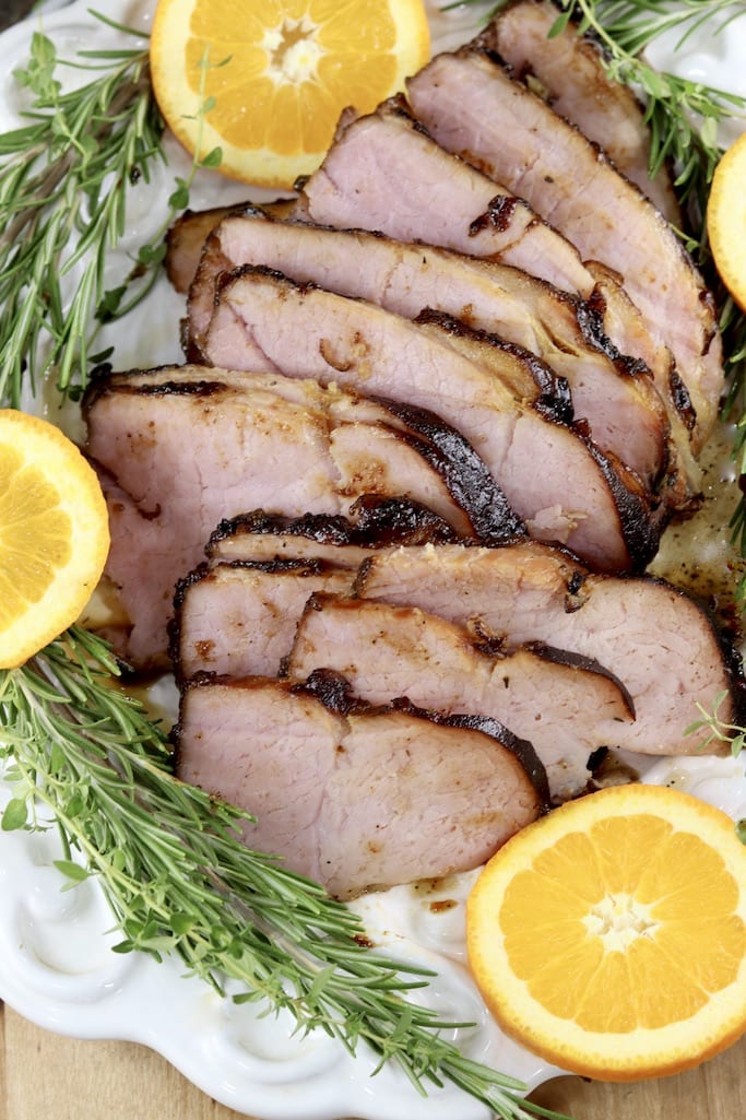 Sliced ham on a platter with rosemary and orange slices