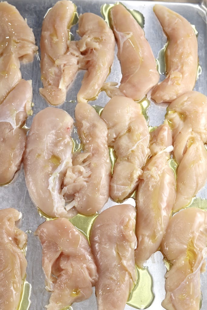 Chicken tenders drizzled with olive oil on a sheet pan