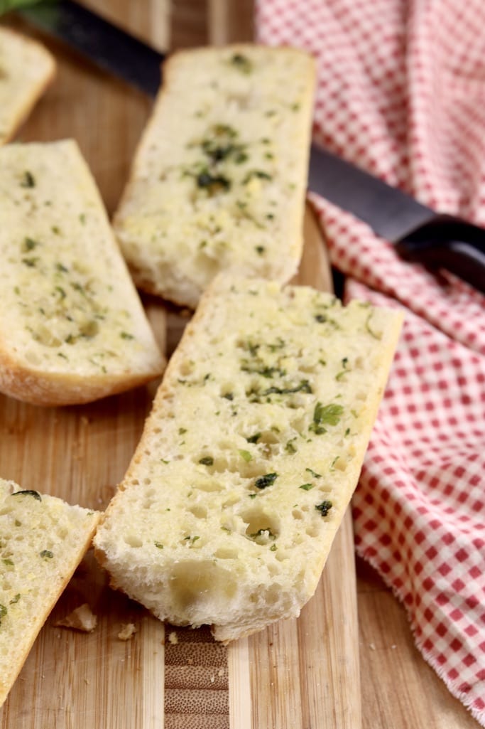 Garlic Bread slices on a cutting board with knife and red napkin