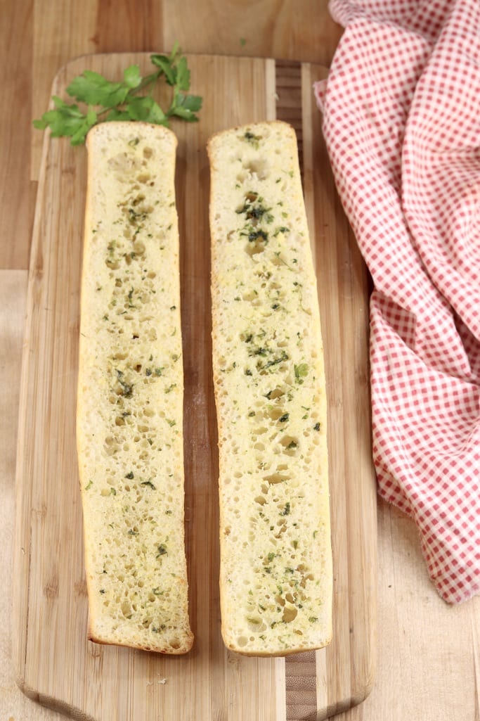 Toasted garlic bread on a wood board with fresh parsley and red napkin