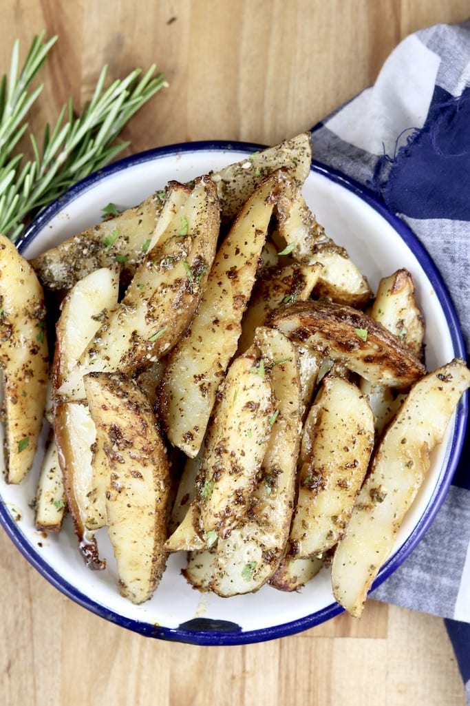 Garlic and Rosemary Roasted Potatoes in a bowl with fresh rosemary and blue check napkin