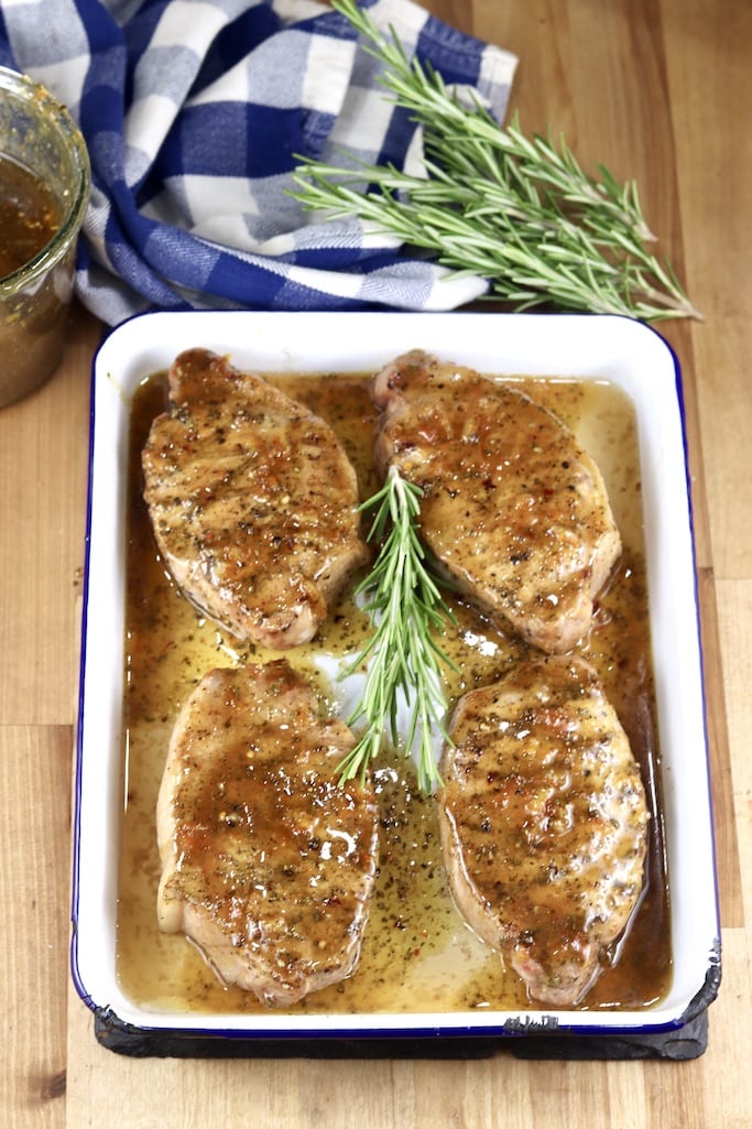 Grilled Pork Chops brushed with Orange BBQ Sauce - 4 on a white baking dish - garnished with rosemary -wood backdrop