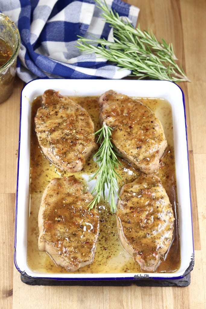 Orange BBQ Sauce over 4 pork chops in a rectangle pan with rosemary garnish