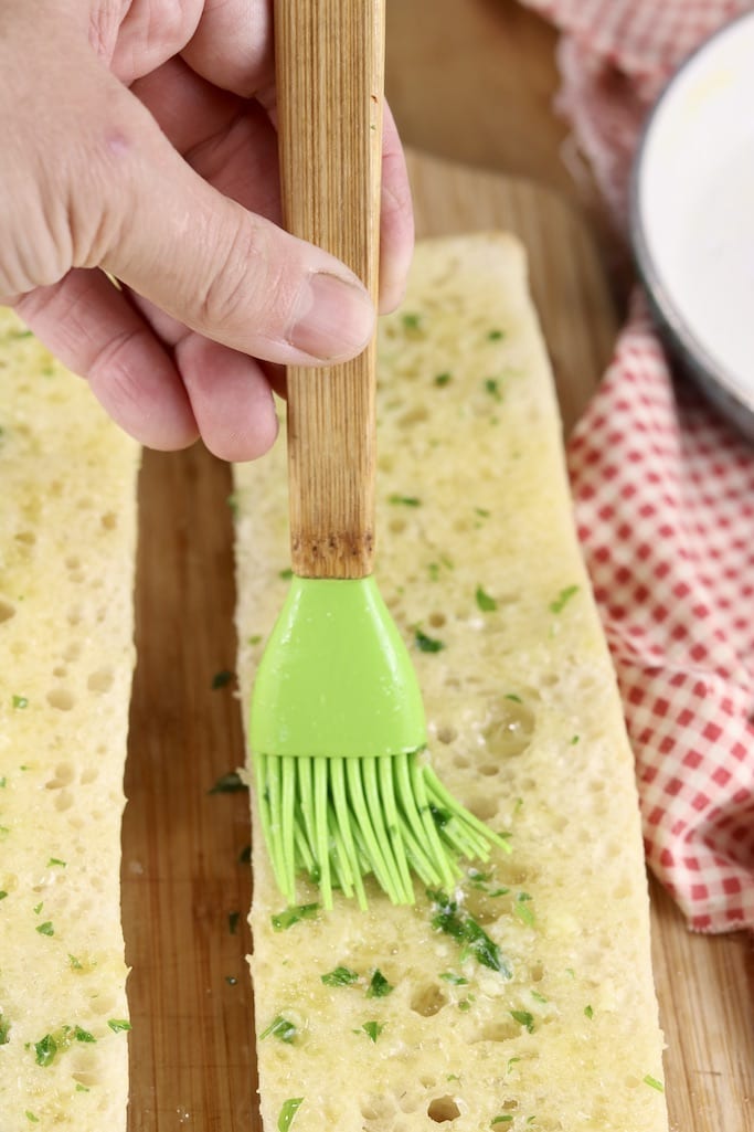 Brushing garlic butter over sliced baguette for grilling