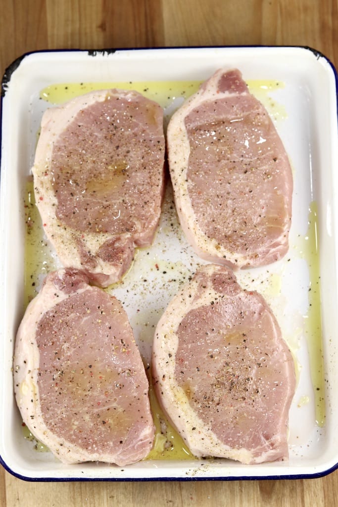 Boneless pork chops with olive oil, salt and pepper on a white pan ready to grill