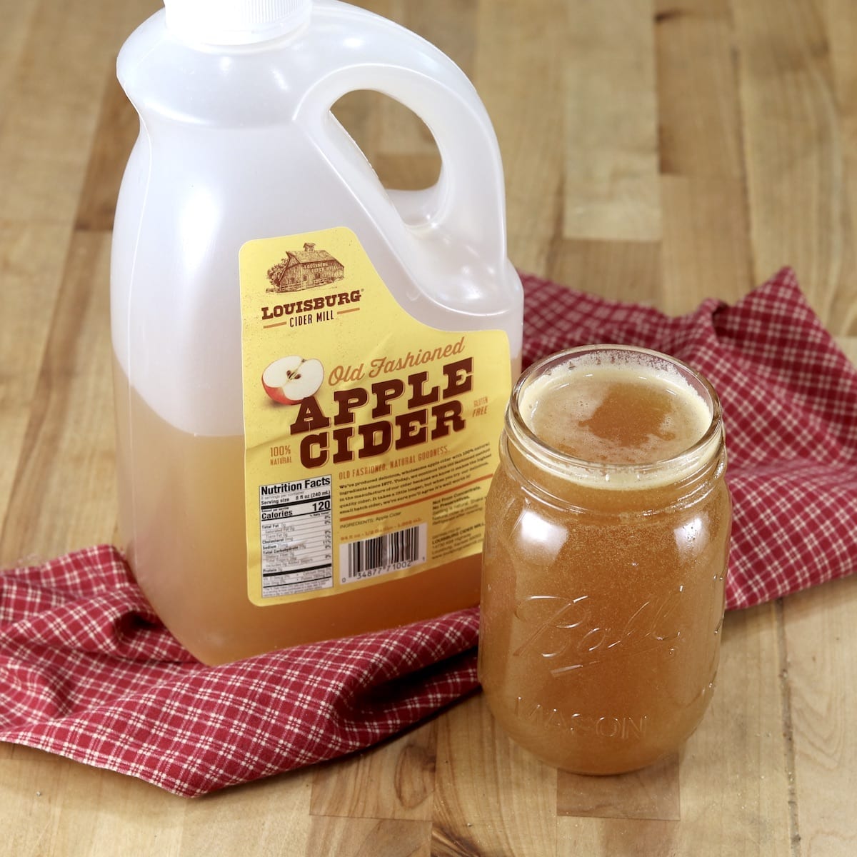 Apple Cider Marinade in a pint jar with jug of apple cider on a red check napkin