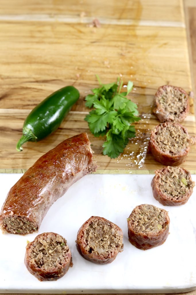 Wood and marble serving board with sliced and link of smoked sausage. Jalapeno and parsley garnish