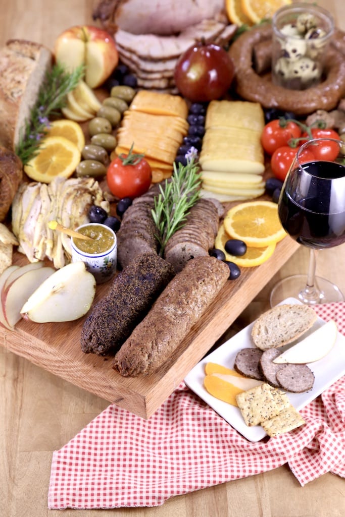 Glass of red wine with meat and cheese grazing board, red napkin, small plate with sausage and cheese