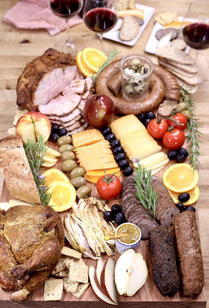 overhead view of smoked meat charcuterie board with cheese, fruit, olives, tomatoes, crackers, bread