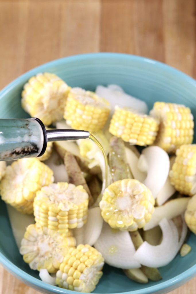Bowl of corn cob chunks, potatoes and sliced onions - drizzled with olive oil