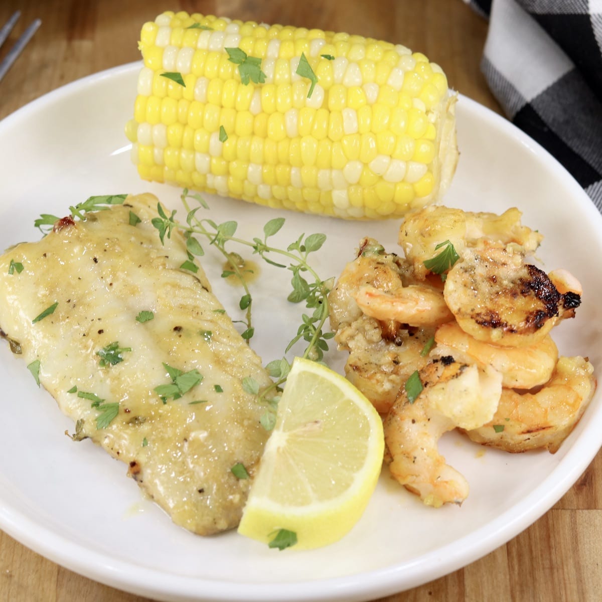 Lemon Garlic Fish and Shrimp with corn on the cob on a plate, lemon wedge garnish