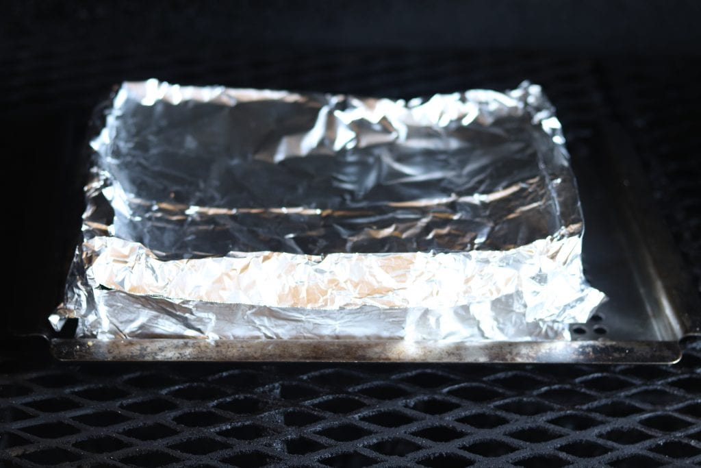 Foil Covered dish of chicken and dressing on grill
