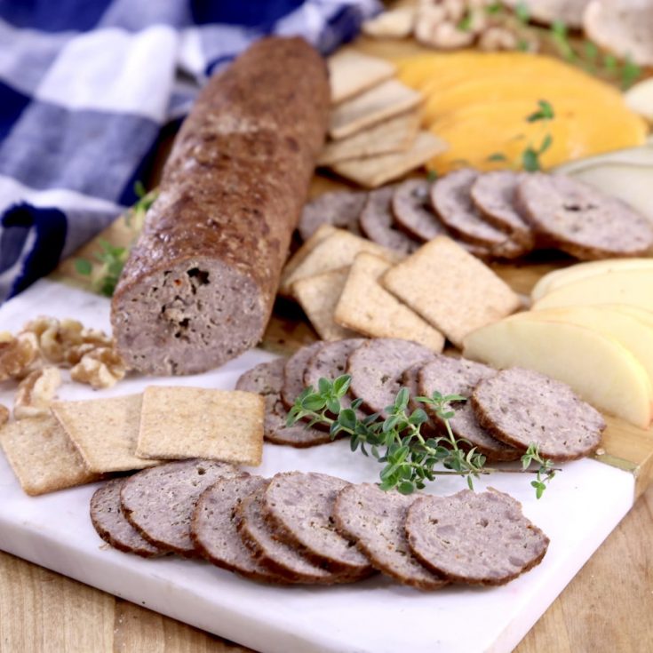 Venison summer sausage sliced on a baord, with cheese, crackers, herbs and nuts