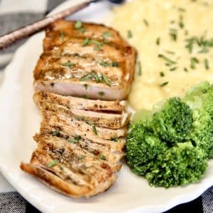 Sliced grilled pork chop on a plate with mashed potatoes and broccoli.