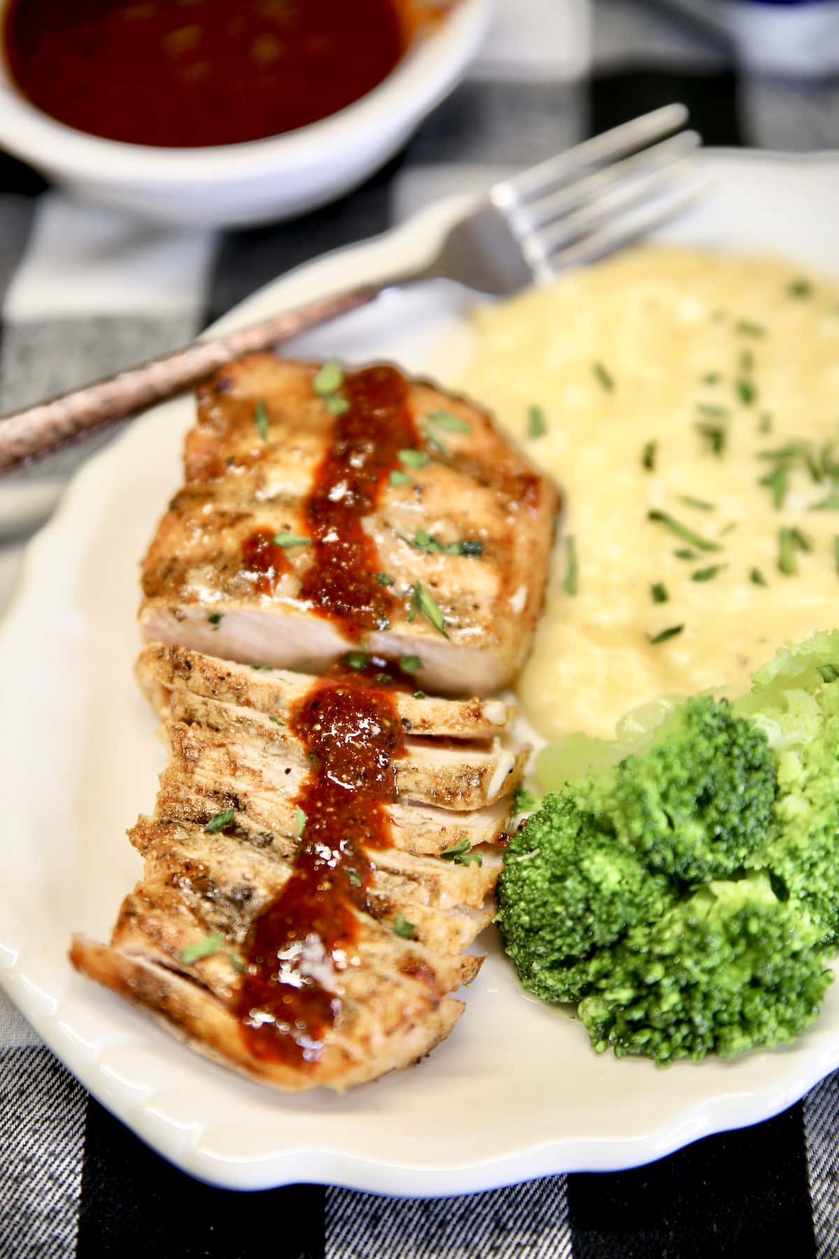 Plate with sliced pork chop drizzled with bbq sauce, broccoli and potatoes.