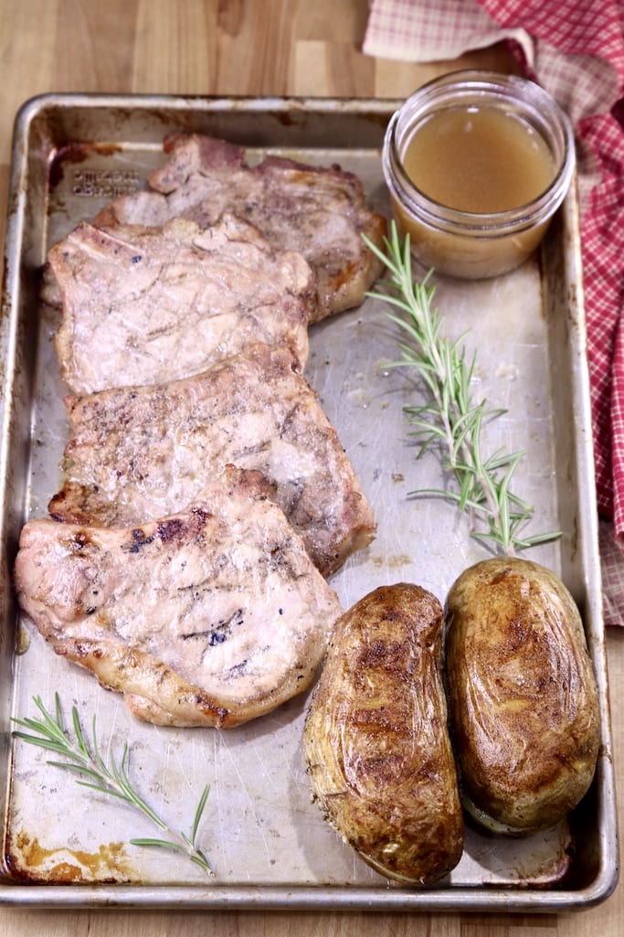 sheet pan of grilled apple cider pork chops and 2 baked potatoes