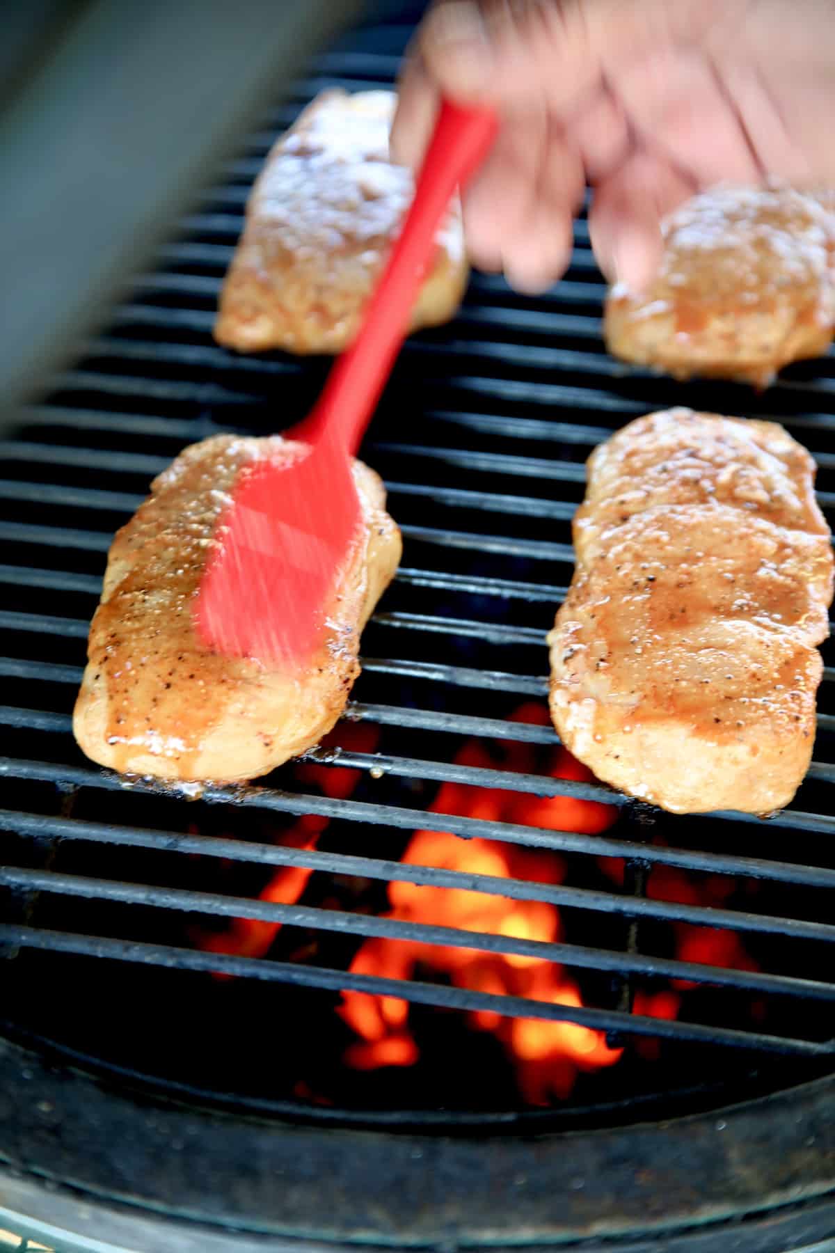 Brushing pork chops with sauce on a grill.