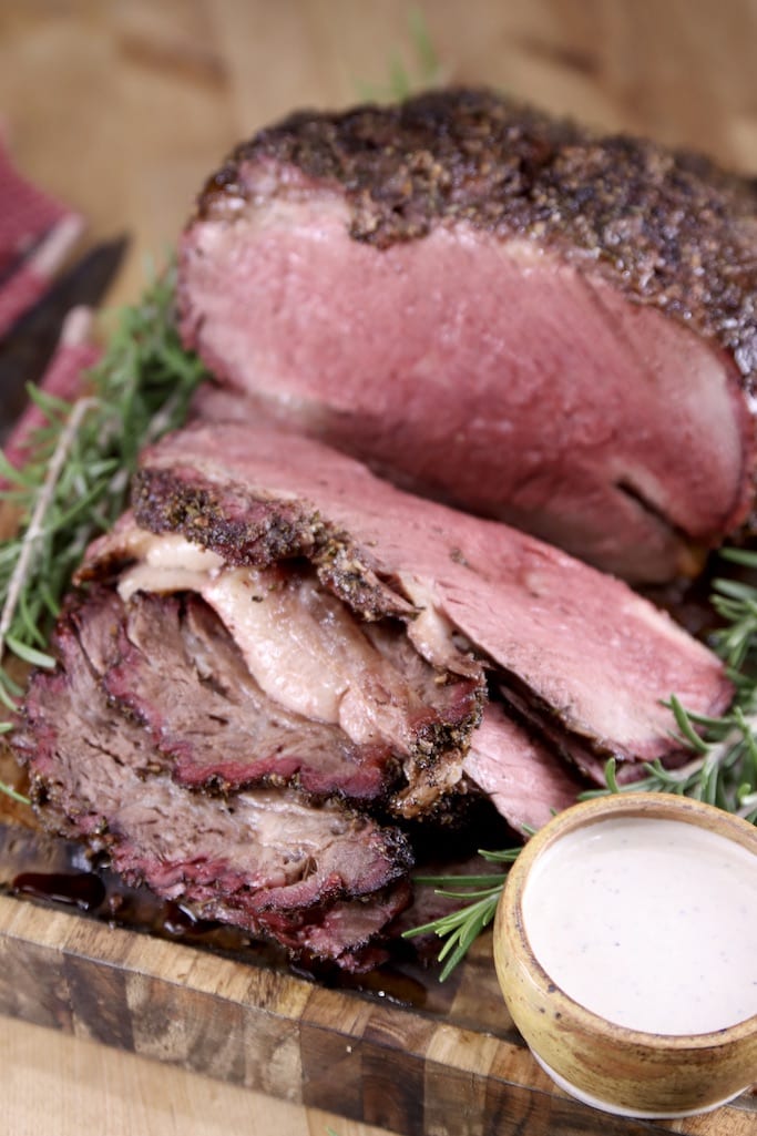 Grilled prime rib on a cutting board with a few slices, horseradish sauce in a small bowl