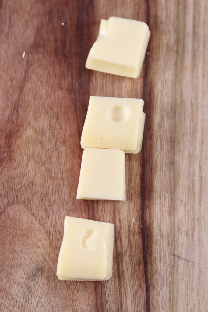 square slices of Jarlsberg Cheese on a cutting board