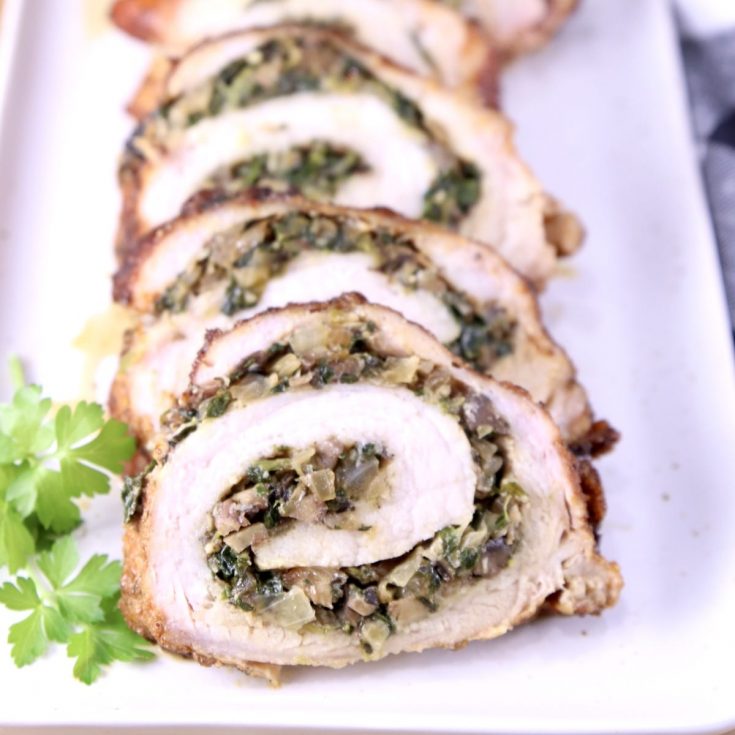 Spinach and mushroom stuffed and grilled pork tenderloin sliced on a platter