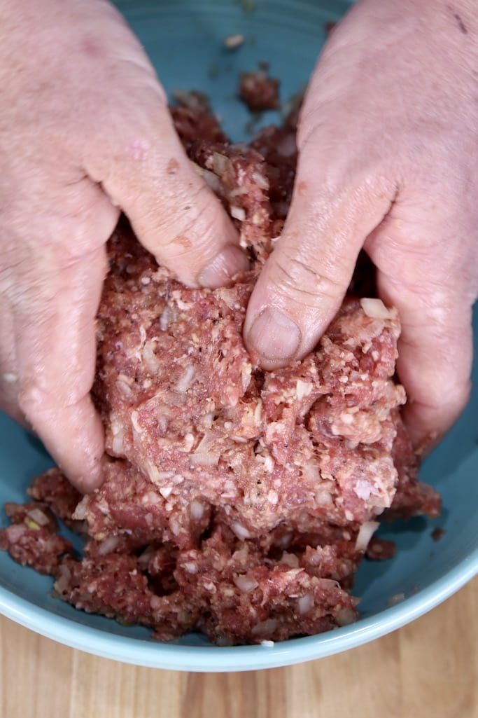 A man's hands mixing ground beef meatball ingredients in a blue bowl