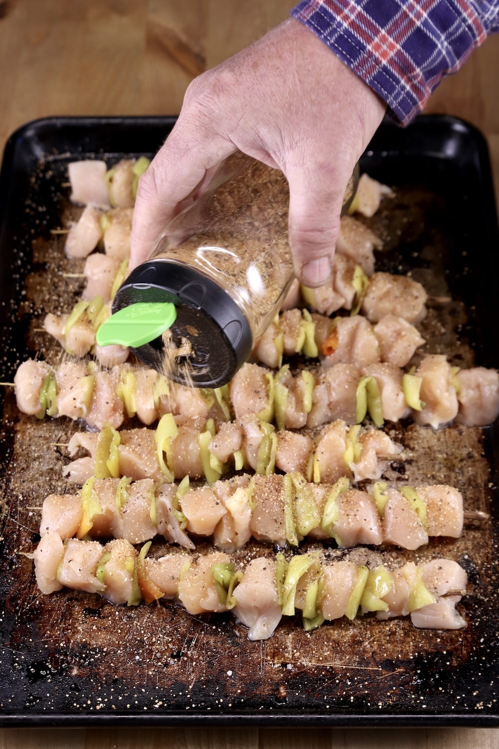 sprinkling dry rub from a jar over chicken skewers on a sheet pan