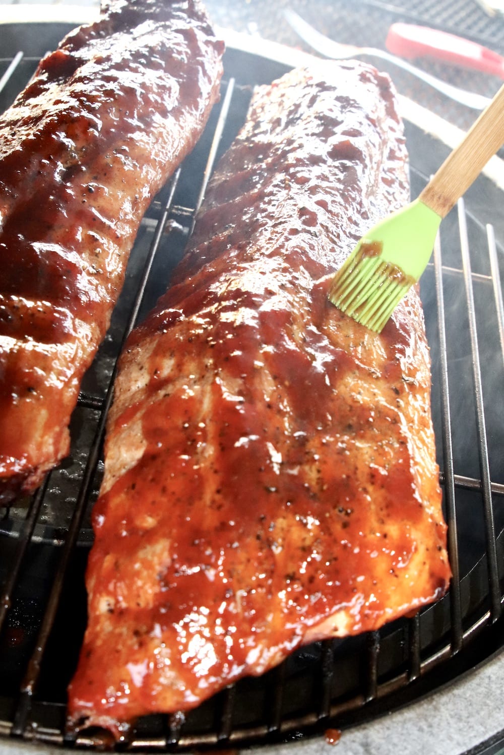 brushing bbq sauce over ribs on a grill