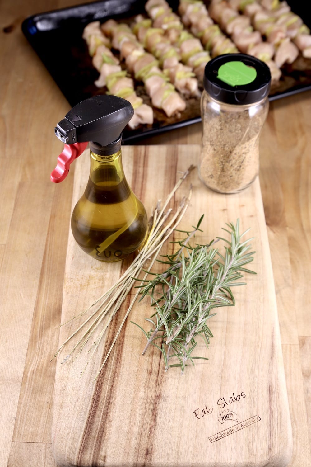 olive oil in a spray bottle, jar of rub, fresh rosemary, chicken kebabs in the background