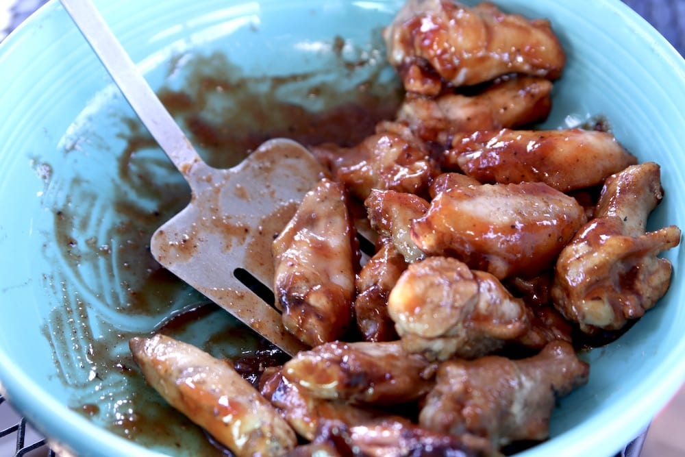 bowl of bbq sauce and chicken wings with a spatula