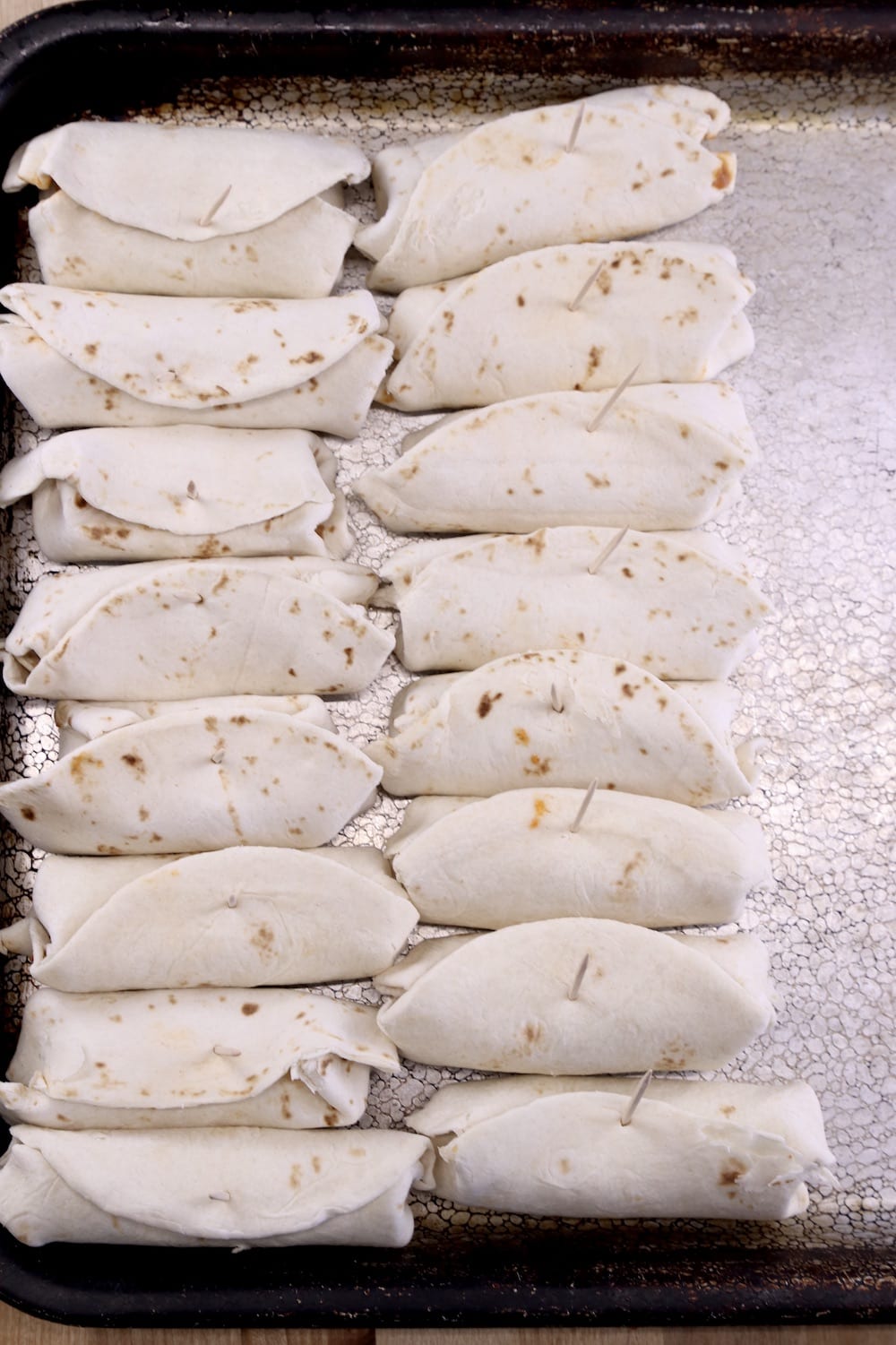 Mini Burritos secured with toothpicks on a sheet pan