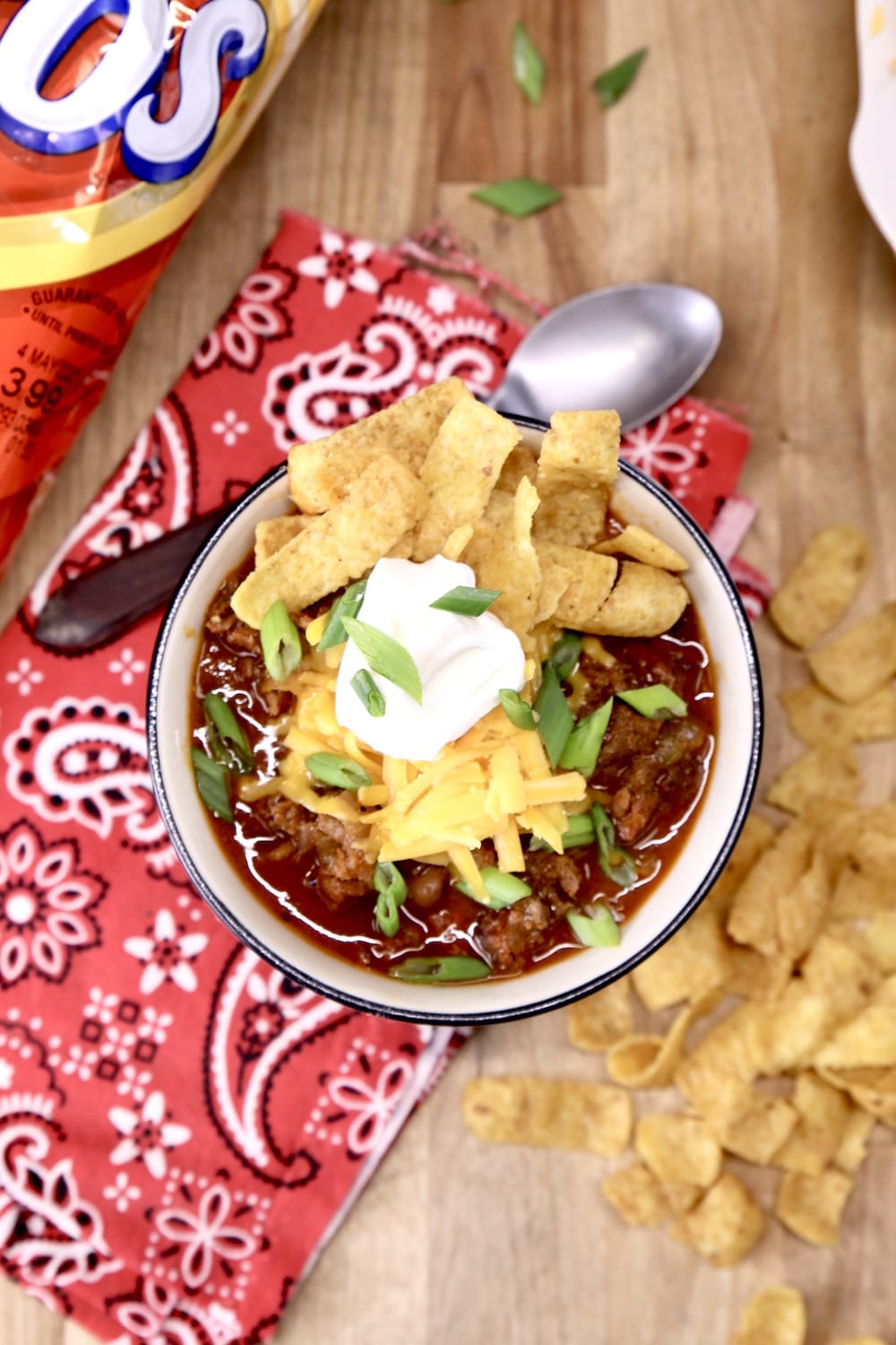 Overhead of bowl of chili with sour cream, cheese and Fritos on a red bandana napkin
