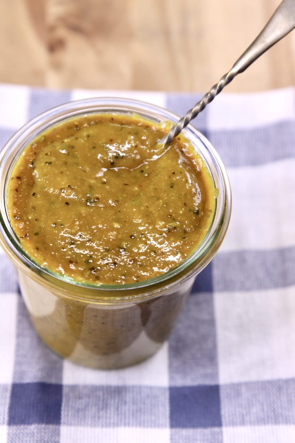 Jar of Rosemary Mustard Sauce with a spoon sitting on a blue stripe towel
