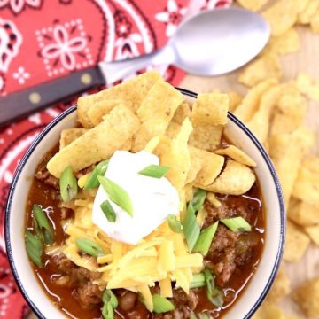 Bowl of chili with a spoon, topped with sour cream, cheese and Fritos