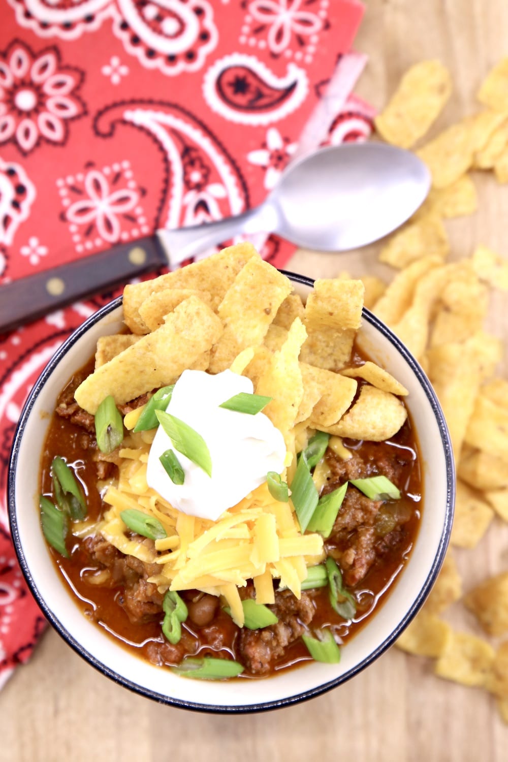 bowl of chili with Fritos, chili, green onions and sour cream. Sitting on a red bandana napkin with a wood handled spoon