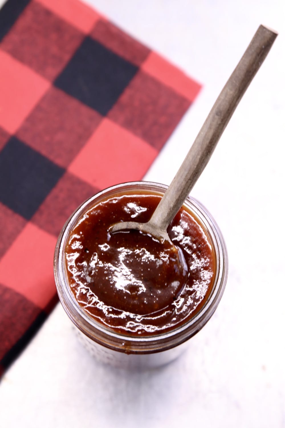 jar of bbq sauce with a wood spoon and buffalo check napkin